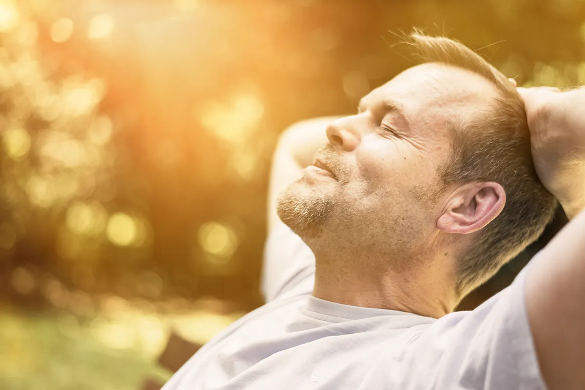 Eine männliche Person auf einer Bank im grünen sitzende gegen das Licht fotografiert