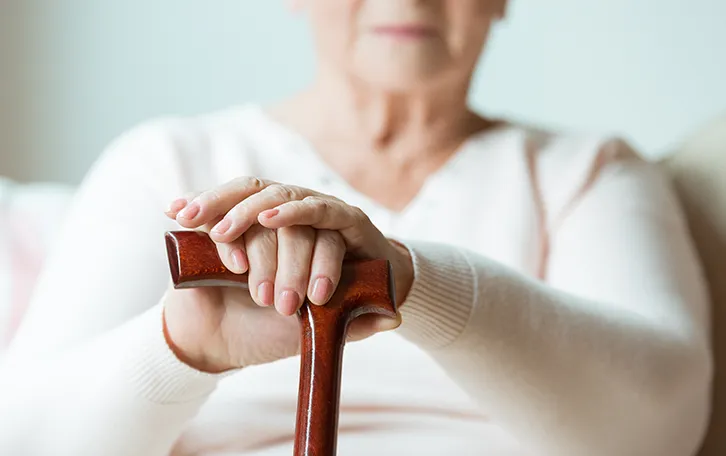 Eine ältere sitzende weibliche Person mit Stock in den Händen
