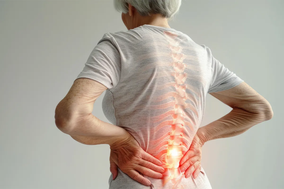 Eine älter Person, die sich den Rücken mit beiden Händen im Beckenbereich hält. Schematisch ist die Wirkelsäule und Rippen dargestellt, Bereiche sind rot hervorgehoben