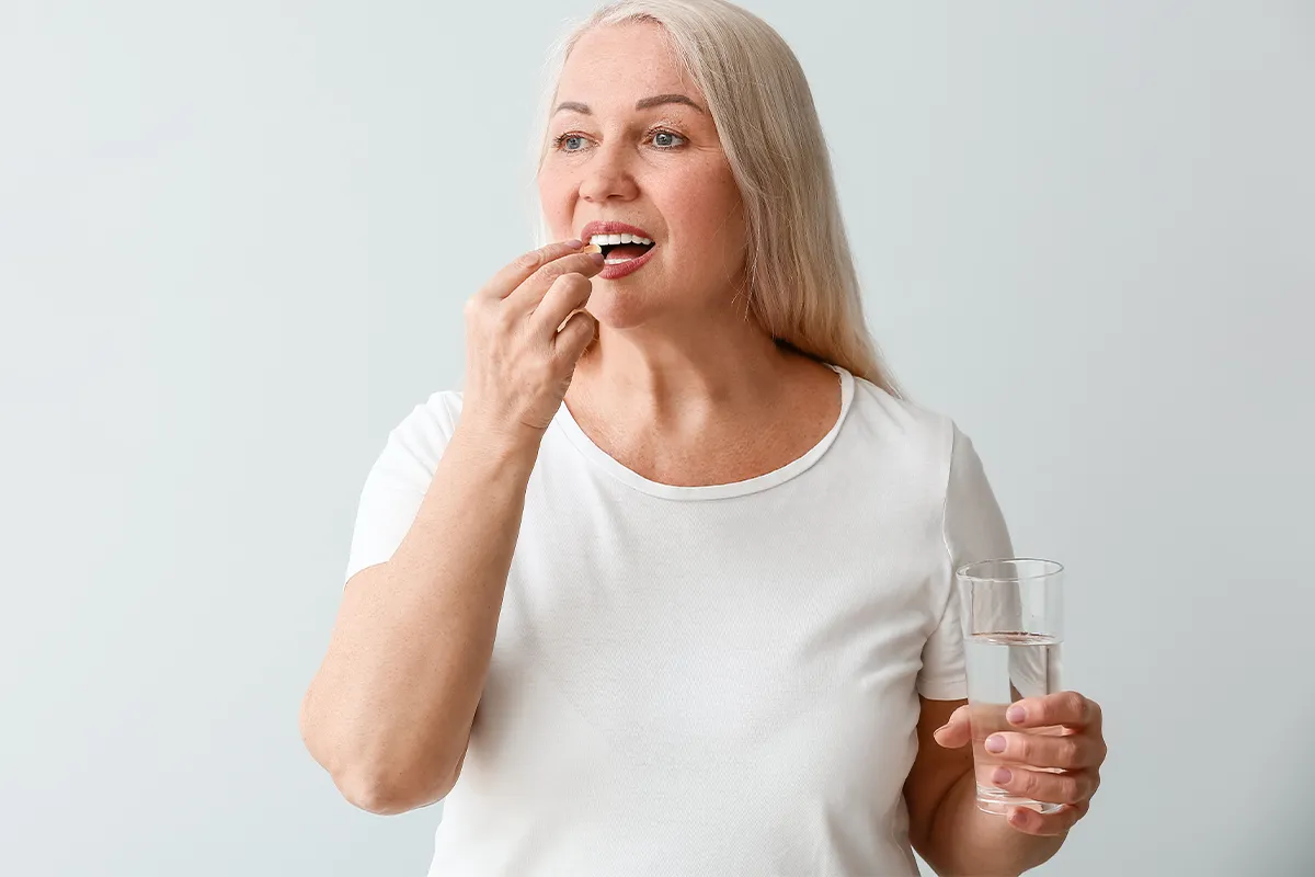 Eine ältere weibliche Person nimmt eine Tablette und hat in der anderen Hand ein Glas Wasser