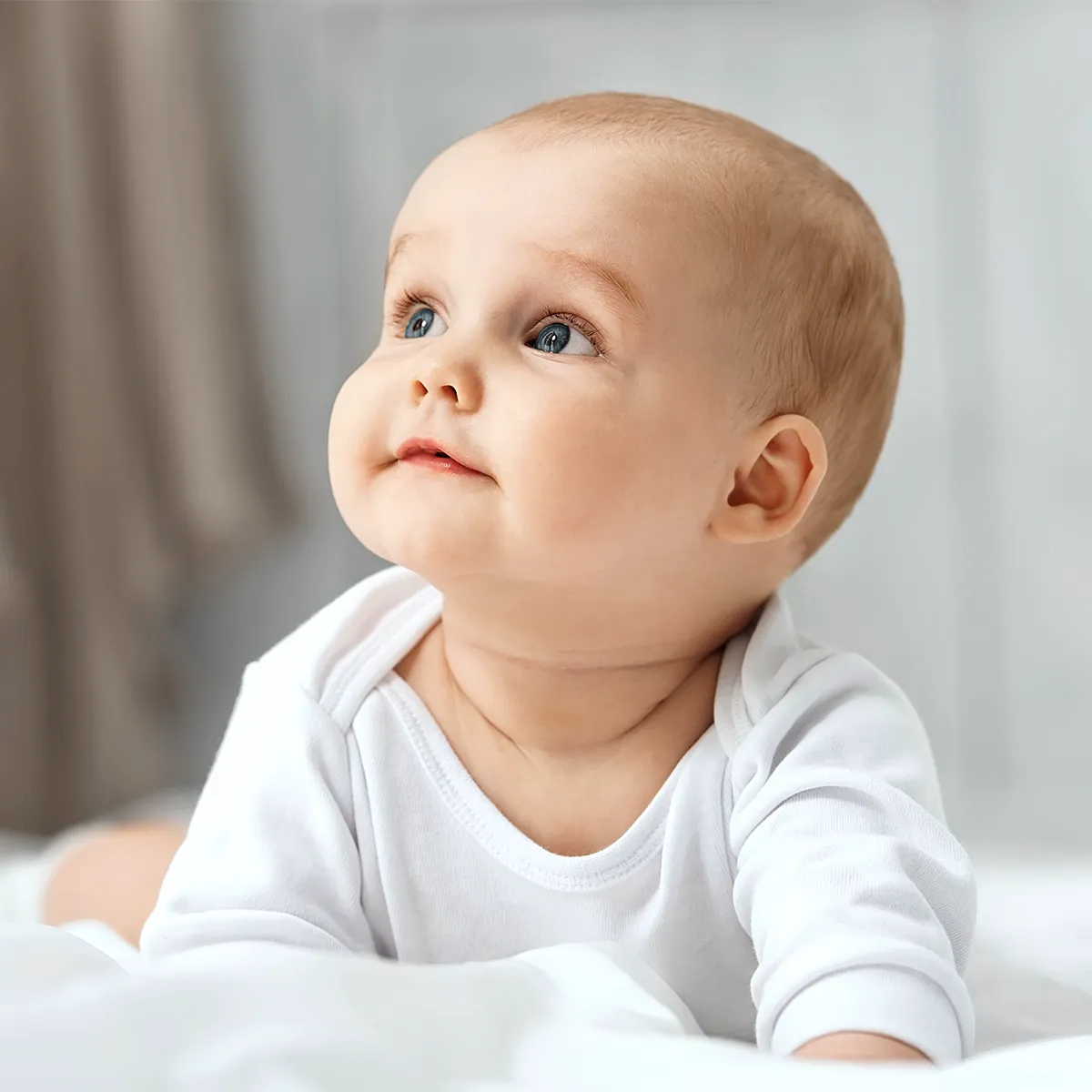 Ein auf dem Bauch liegendes Baby, welches nach oben rechts schaut