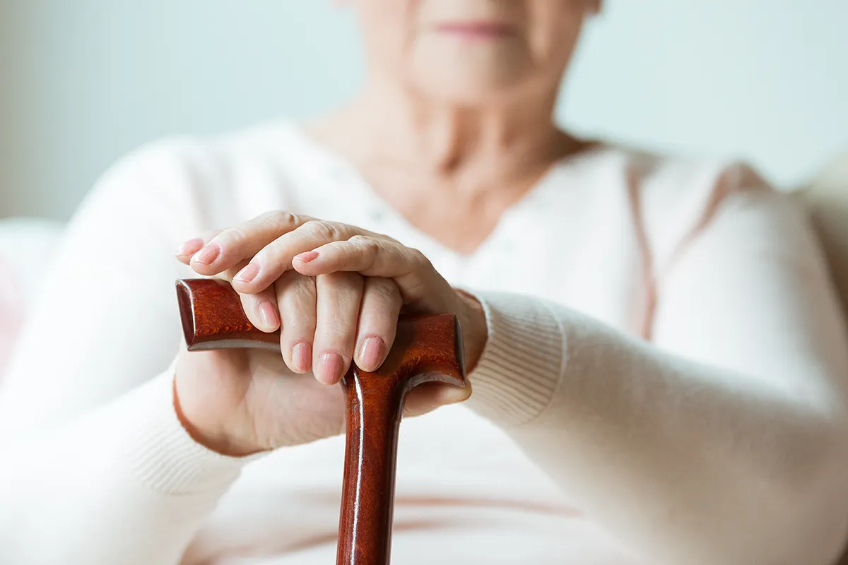 Rolle von Vitamin D im Körper Eine ältere sitzende weibliche Person mit Stock in den Händen