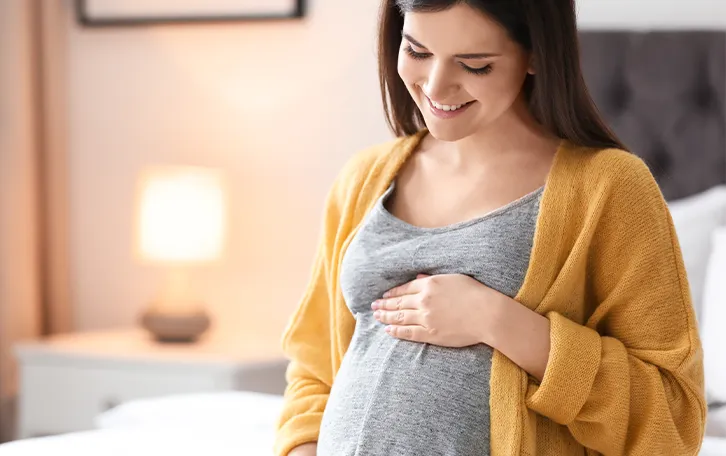 Eine lächelnde Schwangere hält sich den Bauch unterhalt der Brust