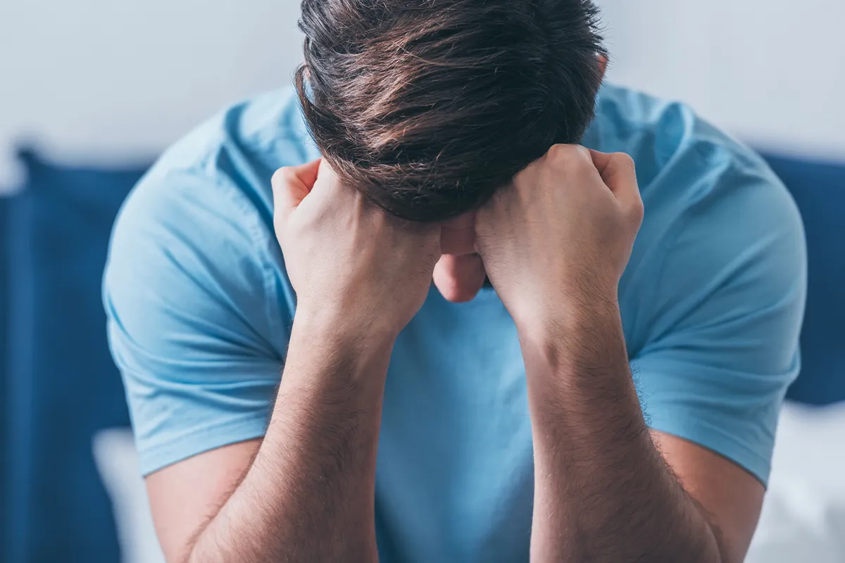 Eine sitzende männliche Person mit dem Kopf auf beiden Fäusten gestützt