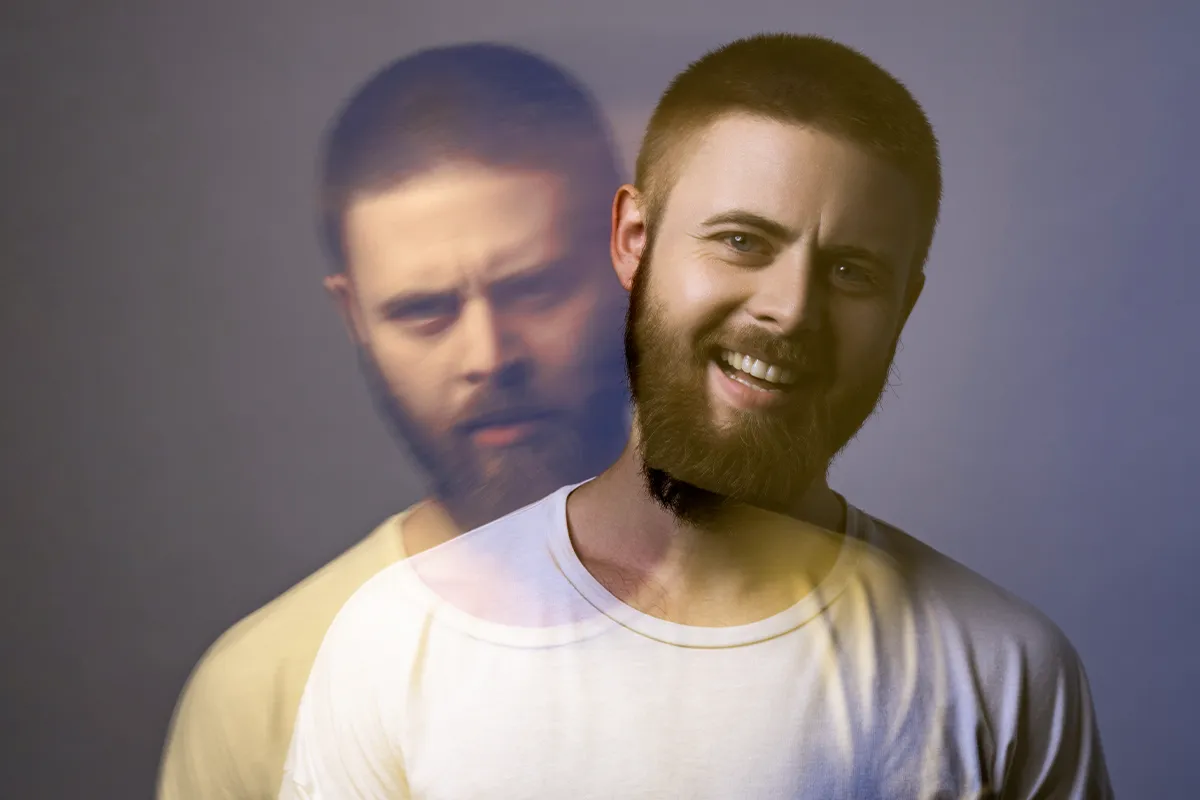 Eine männliche Person in einem doppelt belichtetem Foto. Auf dem einen lächelt er, auf dem anderen schaut er sehr grimmig drein