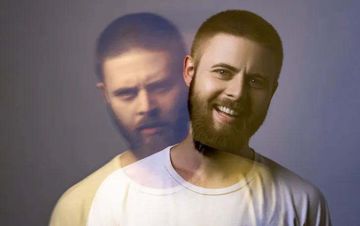 Eine männliche Person in einem doppelt belichtetem Foto. Auf dem einen lächelt er, auf dem anderen schaut er sehr grimmig drein