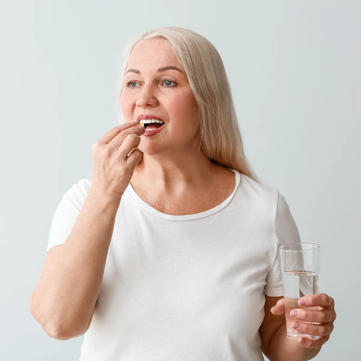 Eine ältere weibliche Person nimmt eine Tablette und hat in der anderen Hand ein Glas Wasser