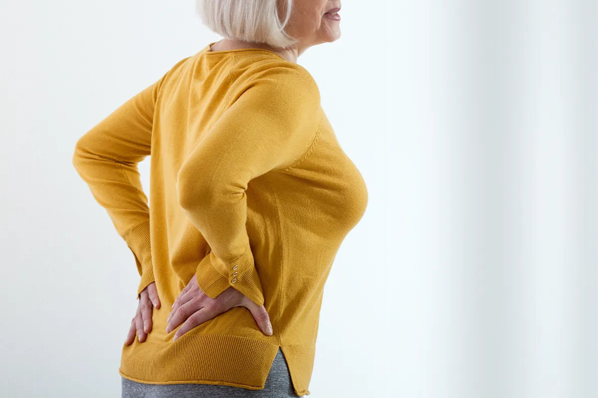 Vit D3 Vitamin D vielseitig einsetzbar Eine ältere weibliche Person hält sich mit beiden Händen den Nieren-/Beckenbereich. Der Mund ist leicht schmerzverzerrt