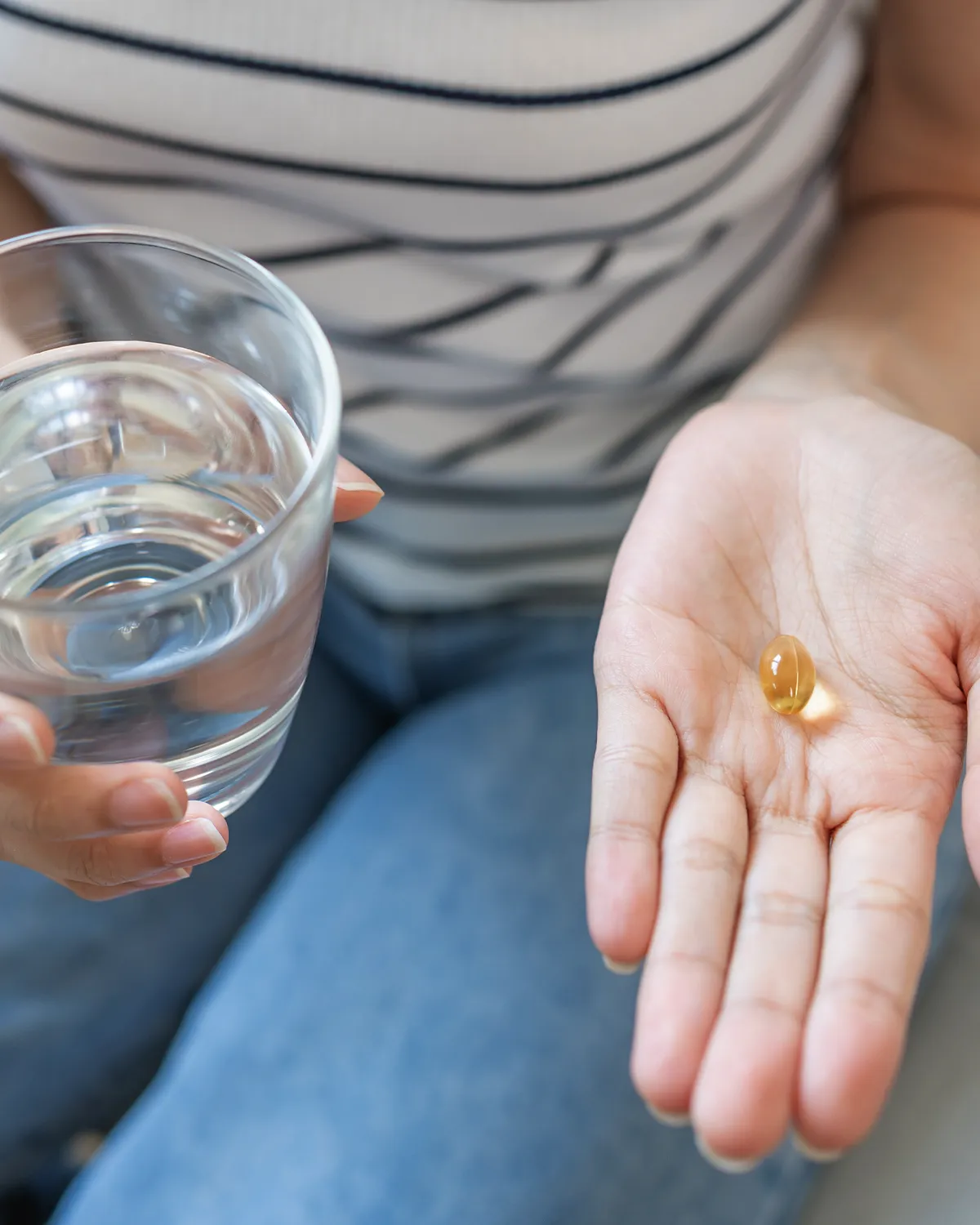 Vit D3 zur Prävention Behandlung Vitamin D Mangel Eine weibliche Person mit einem Glas Wasser in der einen Hand und in der anderen eine tansparente gelbliche Pille
