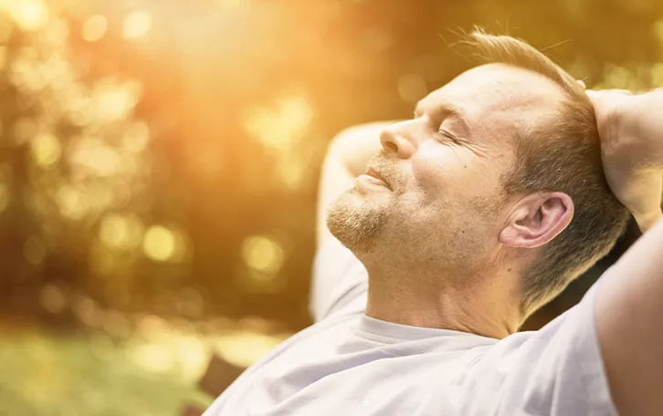 Vitamin D Aufnahme Sonnenlichtquelle Eine männliche Person auf einer Bank im grünen sitzende gegen das Licht fotografiert