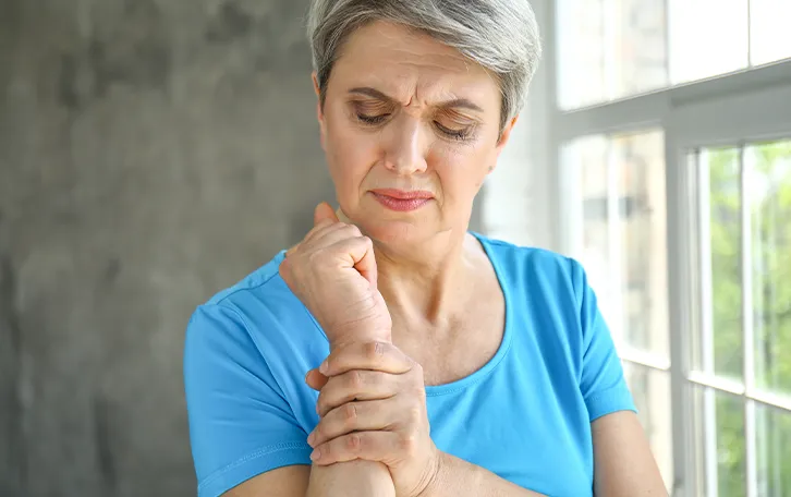 Vitamin D Mangel Symptom Knochenschmerzen Eine stehende ältere weibliche Person hält sich das Handgelenk und schaut komisch darauf