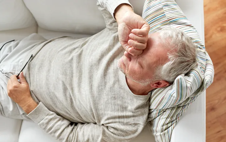 Vitamin D Mangel Symptom Müdigkeit Eine männliche Person auf einer Couch liegend, den Handrücken der einen Hand vor die geschlossenen Augen haltend