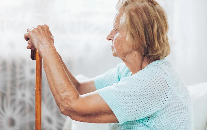 Vitamin D Mangel Symptom Muskelschwäche Das Profil einer sitzenden älteren weiblichen Person, beide Hände auf einen Stock haltend