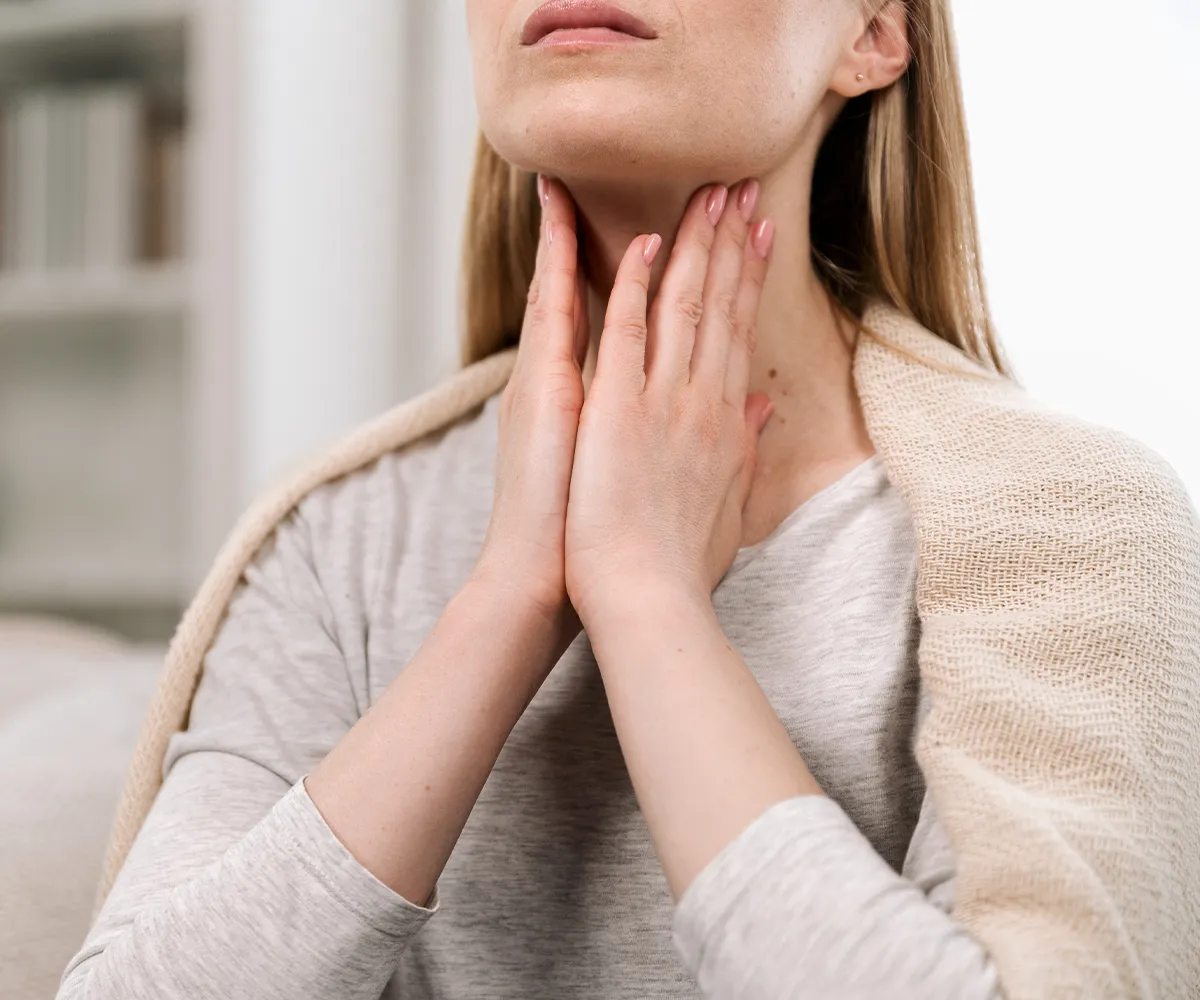 Eine weibliche Person hält sich beide Hände an den Aussenbereich ihres Halses