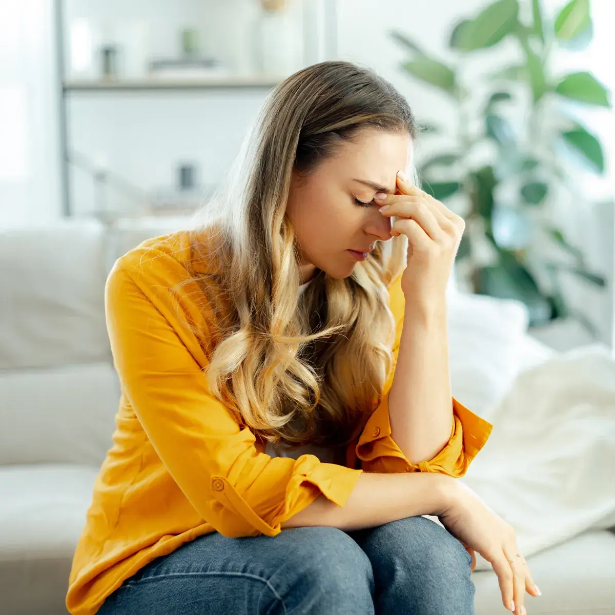 Weitere Symptome durch Vitamin D Mangel Eine weiblich Person mit geschlossenen Augen auf einer Couch sitzend, hält sich mit der einen Hand die Stirn